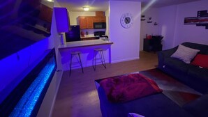 A modern living room with a dark sofa, a red throw pillow, and a kitchen area in the background. - Cozy apartment steps from Christ Hospital, UC and minutes to downtown! (Cincinnati)