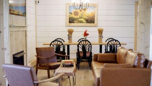 Un salon chaleureux avec une table à manger en bois, deux chaises noires, un canapé en cuir marron et une petite table sur laquelle sont posés des livres.