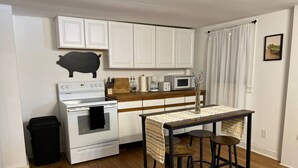 Une cuisine compacte avec des meubles blancs, une cuisinière, un four à micro-ondes et un petit coin repas équipé de tabourets.