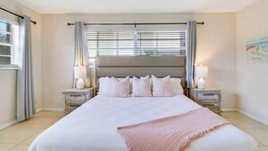 A large bed with a headboard, two bedside tables with lamps, and a window with blinds. - 1 Block to the BEACH! King Beds! BBQ! (West Palm Beach)