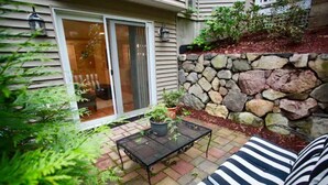 A patio with a stone wall, a metal table, and striped outdoor furniture. - Peaceful 2BR near US Route 1 and Boston. (Melrose)