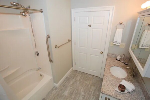 A bathroom with a bathtub, a sink, a mirror, and a door. - Peaceful 2BR near US Route 1 and Boston. (Melrose)