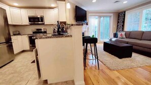 A modern kitchen with white cabinets, stainless steel appliances, and a central island. - Peaceful 2BR near US Route 1 and Boston. (Melrose)