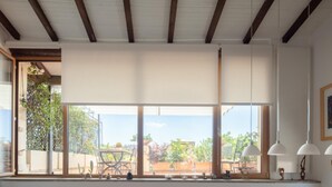 A spacious room with large windows, a dining area with a table and chairs, and a ceiling with exposed wooden beams. - Valeria Terrace   Monti, Rome (ROMA)