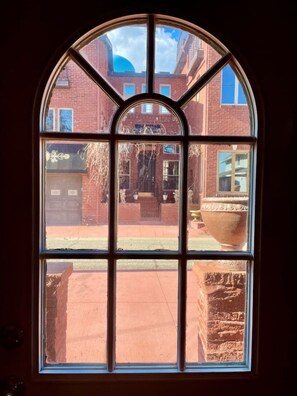A large arched window with multiple panes, offering a view of a brick building and a courtyard with a large planter. - Restored historic log cabin and deck on Lake Erie (Luna Pier)