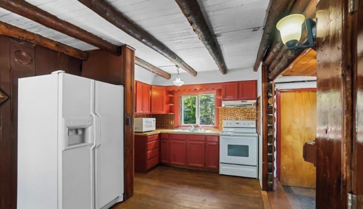 A kitchen with wooden beams, a refrigerator, red cabinets, and a stove.