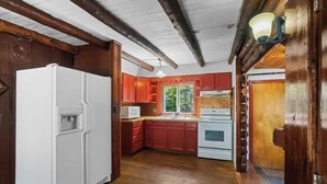 A kitchen with wooden beams, a refrigerator, red cabinets, and a stove.