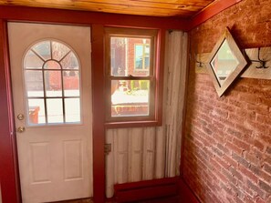 A wooden door with a window, a brick wall, and a small window with a curtain.