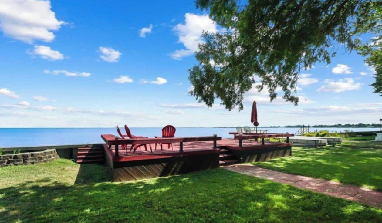 A deck with outdoor seating, a view of the water, and a grassy area.