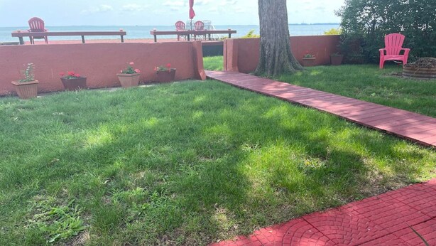 A grassy area with a red brick pathway leading to a seating area with chairs and a table.