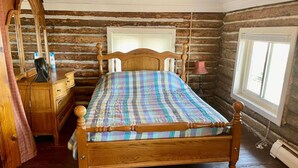 A wooden bed in a log cabin room with a dresser and a mirror. - Restored historic log cabin and deck on Lake Erie (Luna Pier)