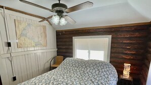 A bedroom with a bed, a ceiling fan, a map on the wall, and a window with blinds.