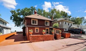 A two-story house with a brick facade, a front porch with potted plants, and a white picket fence. - Restored historic log cabin and deck on Lake Erie (Luna Pier)