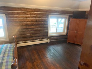 A room with wooden walls, a bed with a plaid bedspread, a window, and a wooden cabinet.