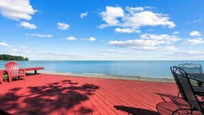 A red deck with a view of a calm lake and distant trees under a partly cloudy sky. - Restored historic log cabin and deck on Lake Erie (Luna Pier)