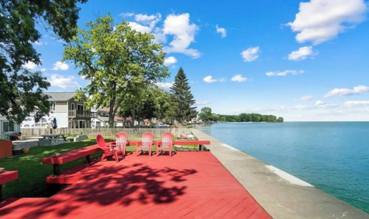 A lakeside deck with red benches and chairs, a concrete edge, and a view of a calm lake and distant trees.