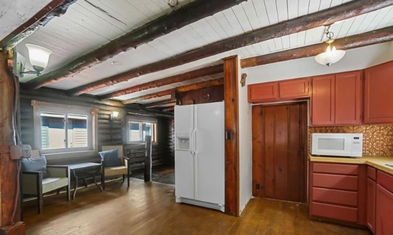 A log cabin interior with a dining area, kitchen, and a large white refrigerator.