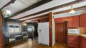 A log cabin interior with a dining area, kitchen, and a large white refrigerator.