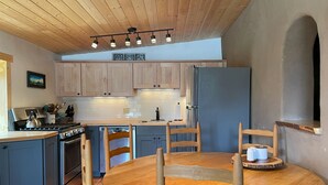 A modern kitchen with wooden cabinets, a built-in oven, a dishwasher, and a round wooden table with chairs. - Ranch House Respite outside Taos, New Mexico! (Carson)