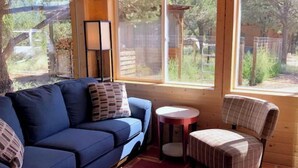 A cozy room with a blue sofa, a plaid armchair, and a small round table. - Ranch House Respite outside Taos, New Mexico! (Carson)
