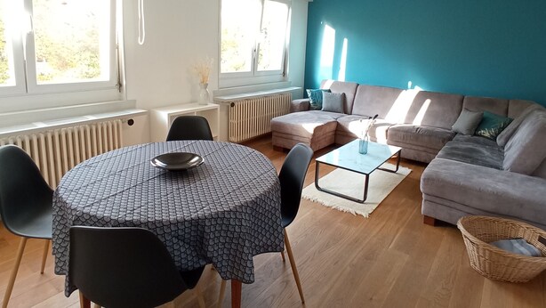 Una sala de estar moderna con una mesa redonda, dos sofás y un amplio ventanal que proporciona luz natural.