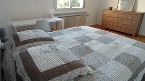 Un dormitorio con una cama grande, un aparador, un escritorio y una ventana con persianas.