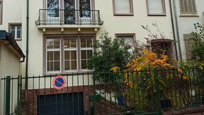 Un edificio residencial de dos plantas con balcón, un letrero de no estacionamiento y una cerca verde.