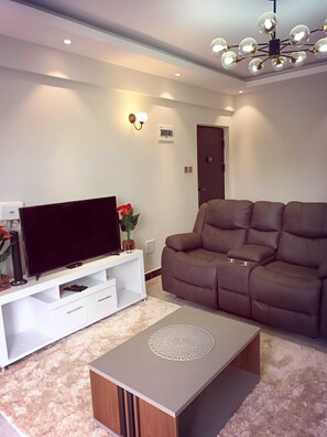 Un salon moderne doté d’un téléviseur à écran plat, d’un canapé marron, d’un meuble de rangement blanc et d’une table basse décorative.