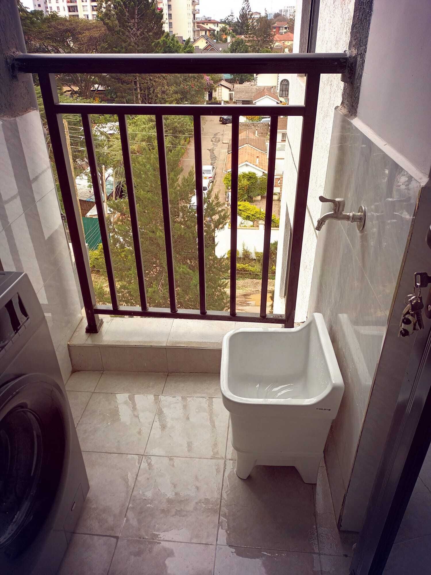 Une petite salle de bain avec des toilettes, un lave-linge et un balcon doté d’une rambarde en métal.