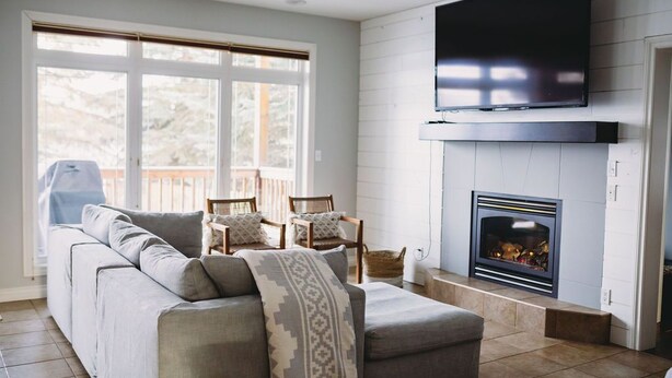 A living room with a grey sofa, two armchairs, a fireplace, and a TV mounted on the wall. - The Lakehouse (Lloydminster)