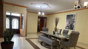 A dining area with a glass table, cushioned chairs, a potted plant, and a chandelier. - AERO-GDL RESIDENCE (Las Pintitas)