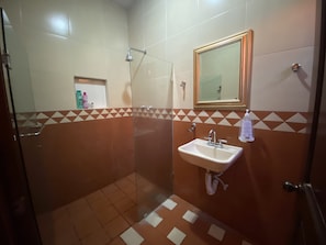 A bathroom with a glass shower enclosure, a sink with a mirror above it, and a tiled floor with a geometric pattern. - AERO-GDL RESIDENCE (Las Pintitas)