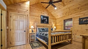 Een slaapkamer in een houten chalet, met een bed, bedlampen, een plafondventilator en een ingelijst foto aan de muur.