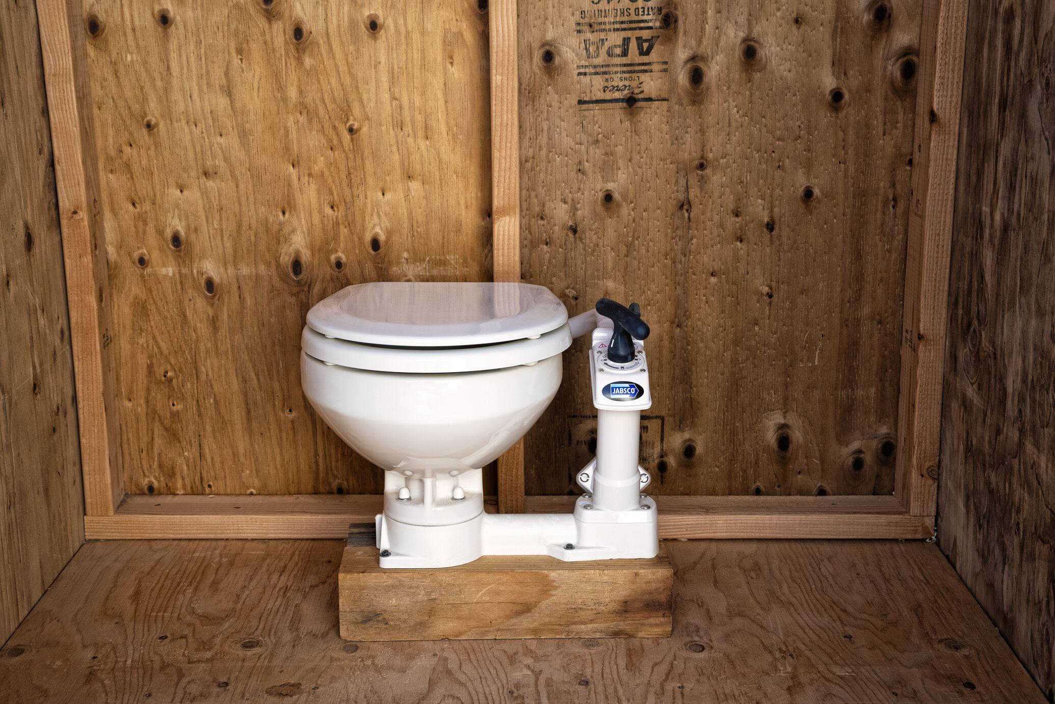 A white toilet with a bidet attachment in a wooden stall.