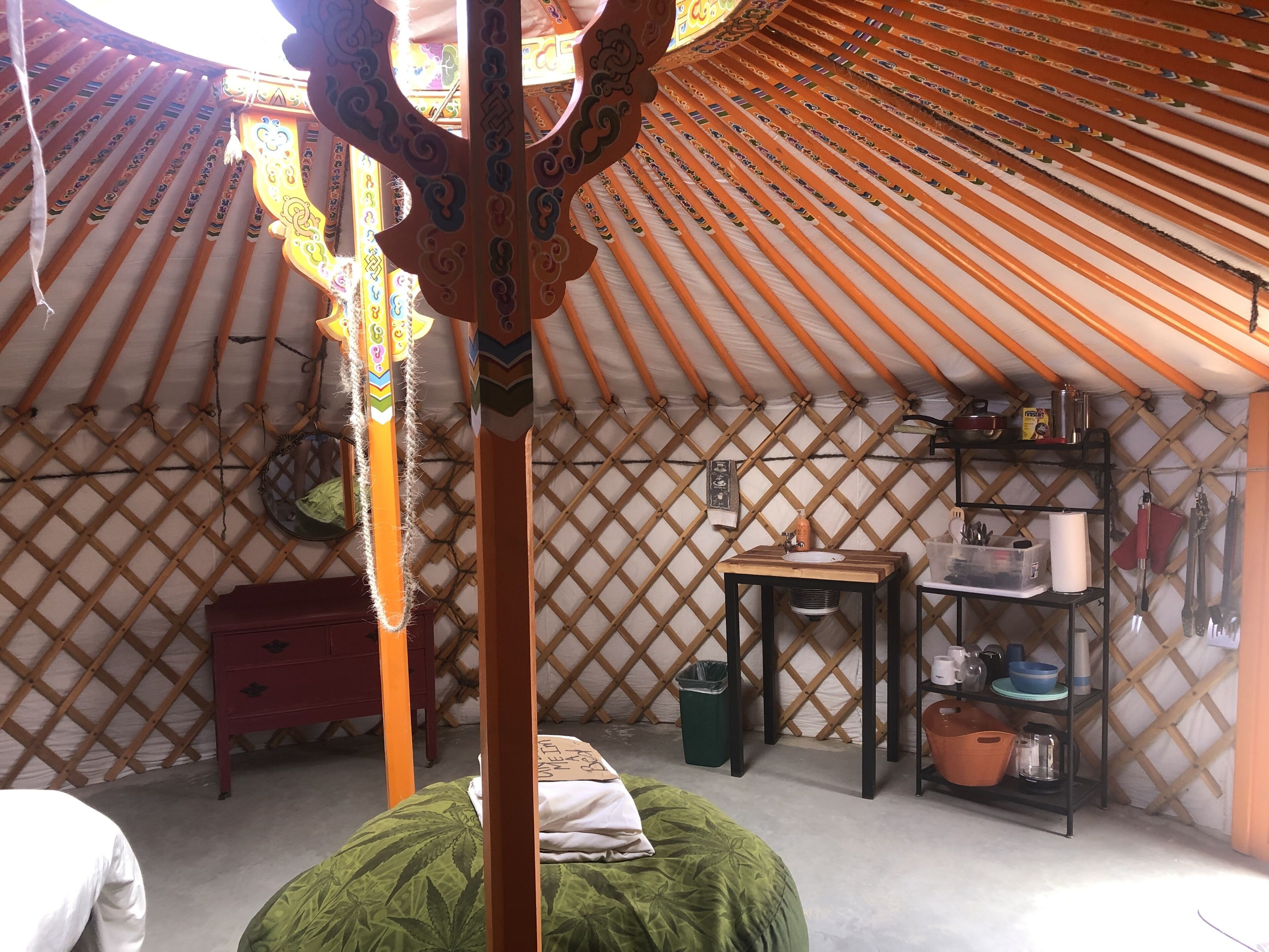 A traditional yurt interior with a bed, a small table, and a shelf with various items.