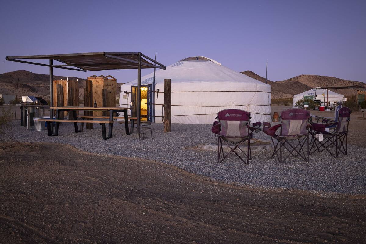 A yurt with a wooden structure in front, a table with chairs, and a gravel ground.