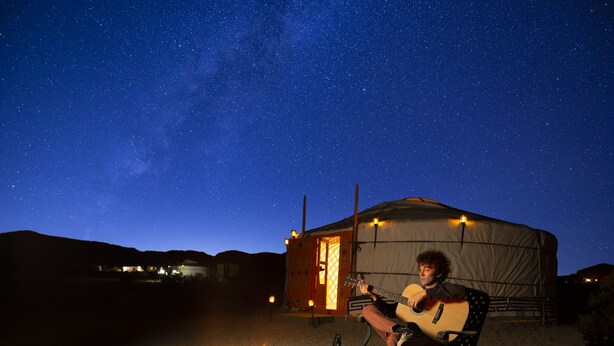 A person sitting by a campfire in front of a tent under a starry night sky. - 28 Palms Ranch (Twentynine Palms)