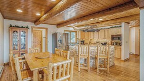 Tilava keittiö, jossa on puiset kaapit, keskeinen keittiösaareke ja ruokailutila puutuoleineen.