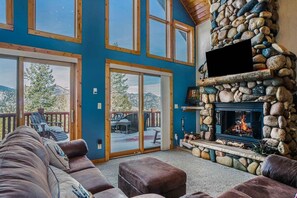 A spacious living room with a stone fireplace, large windows, and a view of the outdoors.