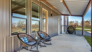 A covered patio area with two rocking chairs and a table, large windows, and a metal gate.