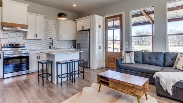 A modern kitchen with white cabinets, a central island with stools, a stainless steel oven, and a refrigerator.