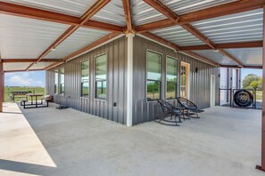 Un espacio al aire libre techado con techo metálico, ventanas amplias y suelo de hormigón.