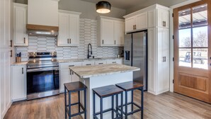 A modern kitchen with white cabinets, a stainless steel refrigerator, and a wooden island with bar stools.