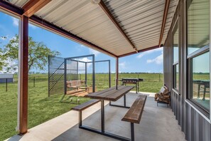 Un patio al aire libre con una mesa y bancos de madera, una parrilla y vistas al campo.