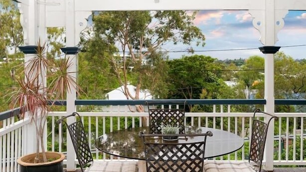 A covered outdoor area with a round glass table and metal chairs, surrounded by white railings and potted plants. - The Indooroopilly Queenslander 4BDR Home (Indooroopilly)