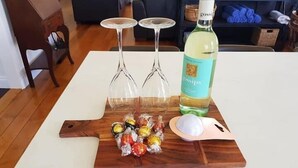 A wooden board with two wine glasses, a bottle of liquor, and a bowl of snacks on a white table. - The Indooroopilly Queenslander 4BDR Home (Indooroopilly)