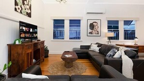 A modern living room with a sectional sofa, a coffee table, a TV, and a bookshelf. - The Indooroopilly Queenslander 4BDR Home (Indooroopilly)