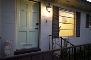 Una casa con puerta blanca, luz exterior encendida y ventana con contraventanas.