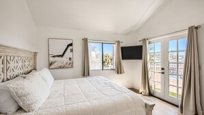 A bedroom with a large bed, a window with curtains, a mounted TV, and a view of buildings outside. - 1 Block to Beach/Restaurants/Bars, Remodeled, 2-Car Garage w/fee, Yard, Sleep 10 (San Diego)