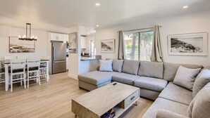 A modern living room with a sectional sofa, a dining table with chairs, a kitchen area, and artwork on the walls. - 1 Block to Beach/Restaurants/Bars, Remodeled, 2-Car Garage w/fee, Yard, Sleep 10 (San Diego)
